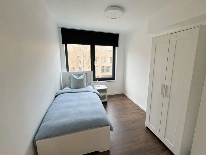 Einzelzimmer mit Bett, Kleiderschrank und großem Fenster